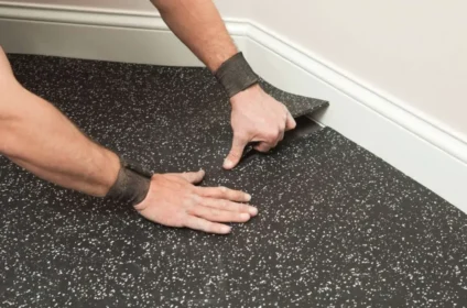 Installing the black speckled rubber mats in a corner with white baseboard